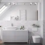 Widok na ścianę w łazience z dużym lustrem, umywalką i sedesem