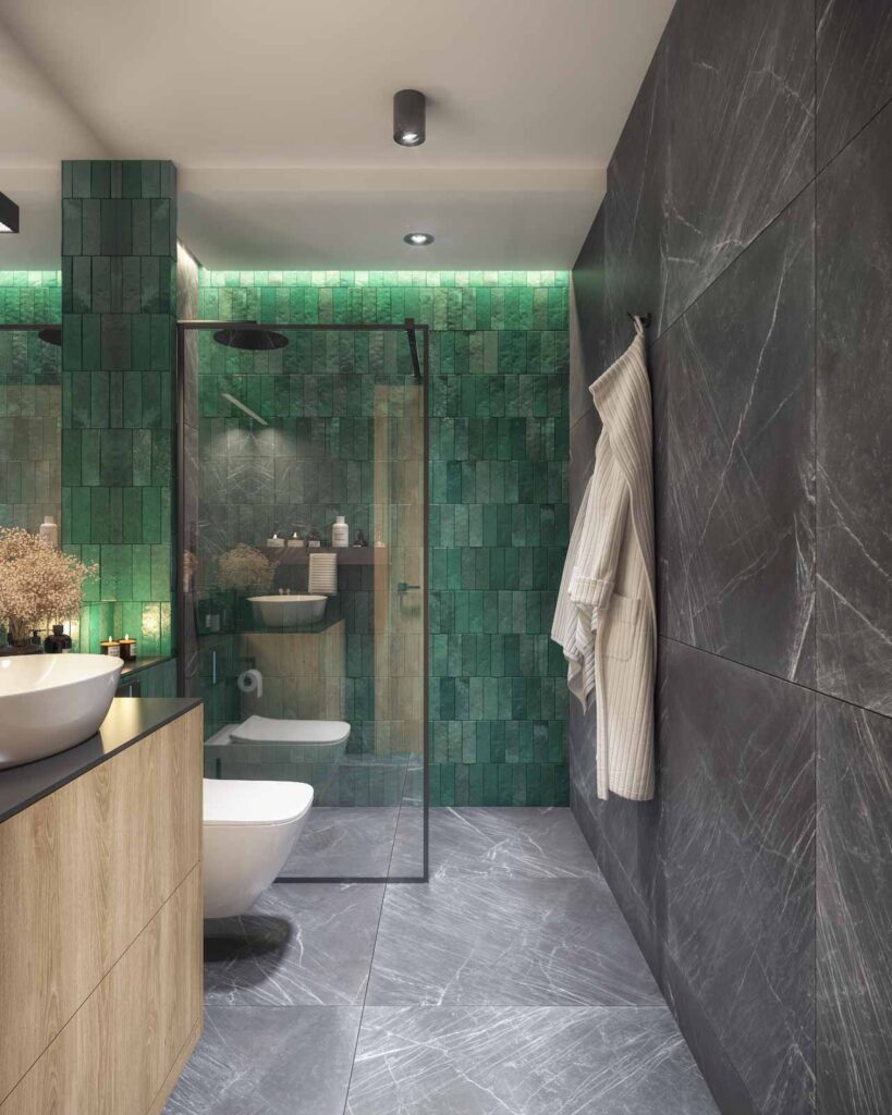 Widok na luksusową łazienkę z ciemnym marmurem na ścianach i podłodze, zielonymi płytkami w obszarze prysznica, przezroczystymi drzwiami kabiny, drewnianymi meblami oraz minimalistycznym wyposażeniem.